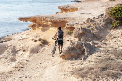 Rear view of man walking on rock by sea