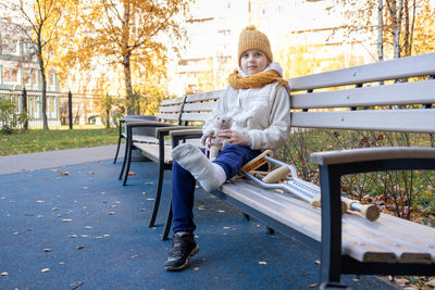 Kid walks in autumn park on crutches. child sitting on park bench. girl has one leg broken in cast.