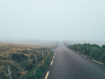 Road amidst landscape against sky during foggy weather