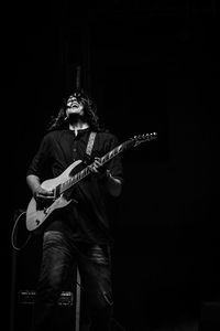 Singer playing guitar while singing against black background