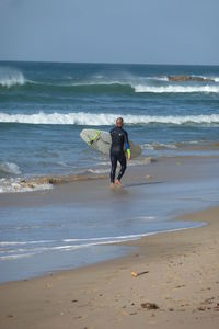 Rear view full length of man walking with surfboard at beach