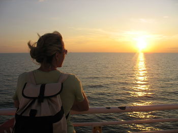 Rear view of woman standing on cruise ship in sea against sky during sunset