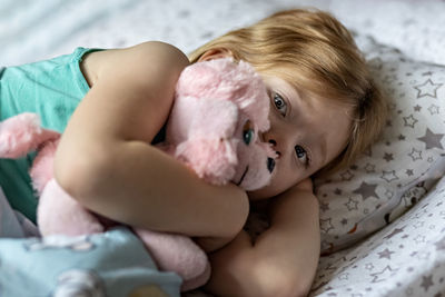 Portrait of cute baby girl with stuffed toy lying on bed at home