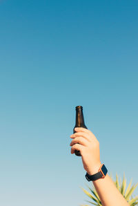 Vertical shot of bottle lifted high on blue sky background