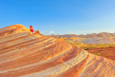 Side view of mature woman sitting on rock formations against blue sky during sunset