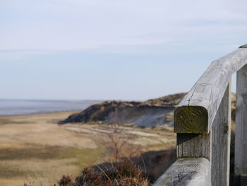 Close-up of wooden post on land by sea against sky