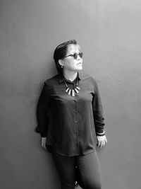 Woman in sunglasses and necklace standing against wall