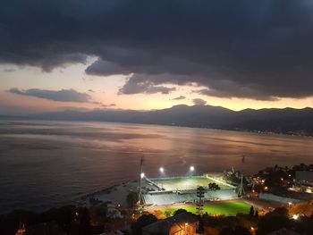 High angle view of illuminated city by sea against sky at sunset