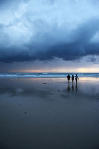 Silhouette people standing on beach against sky during sunset