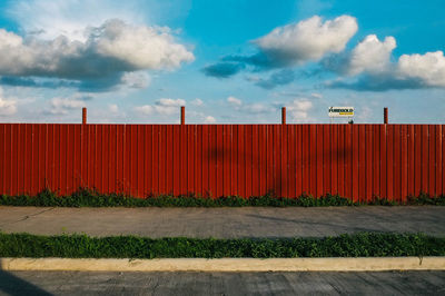 Street by red fence against sky