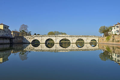 Arch bridge over river against clear blue sky