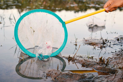 Cropped hand of boy removing bottle from net floating in lake