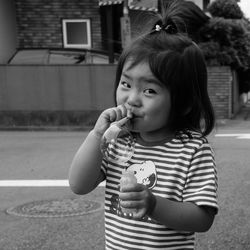 Portrait of cute girl blowing soap bubble while standing against house