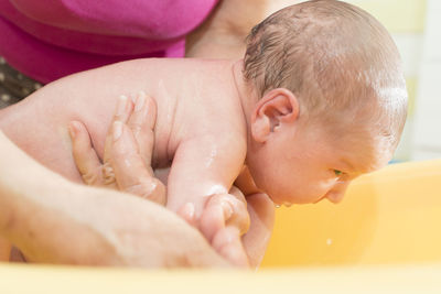 Close-up of grandmother bathing shirtless baby girl in bathtub at home