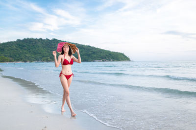 Rear view of woman standing at beach against sky