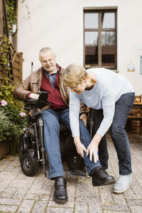 Full length of senior woman helping man with disability sitting in motorized wheelchair at back yard