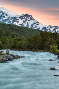 Scenic view of river by mountains against sky during sunset