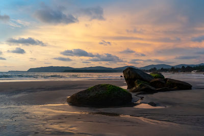 Rocks on beach against sky during sunset