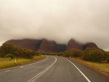 Empty road by mountains against clear sky