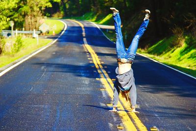 Woman doing handstand on road during sunny day