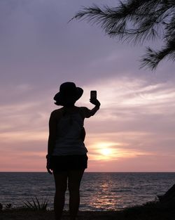 Rear view of woman standing at beach against sky during sunset