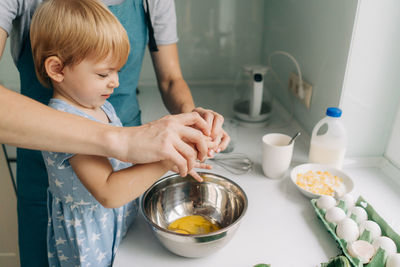 Mom teaches her daughter to break eggs into a bowl for cooking dinner.