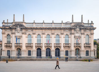 People walking in front of historical building against sky