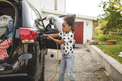 Girl charging electric car while standing on driveway