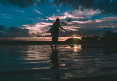 Silhouette person standing in sea against sky during sunset