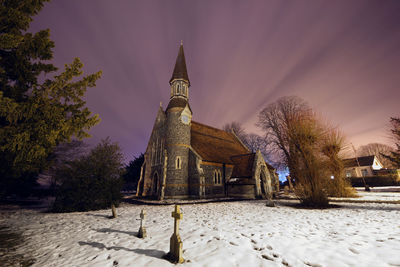 Tombstones on snow covered cemetery by church during winter