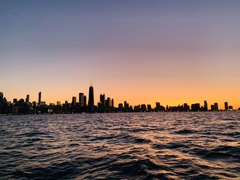 Sea and buildings against sky during sunset