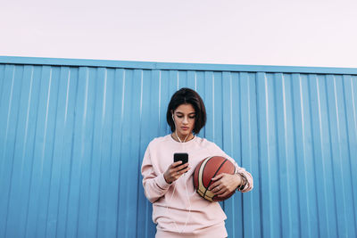 Young man using smart phone while standing against wall