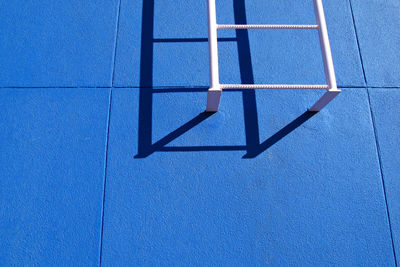 Low angle view of white ladder on blue wall during sunny day