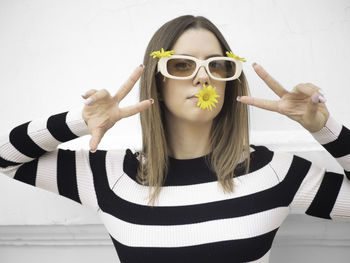 Portrait of young woman wearing sunglasses against wall