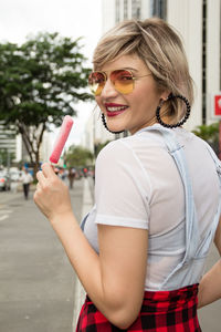 Portrait of smiling woman holding ice cream standing outdoors