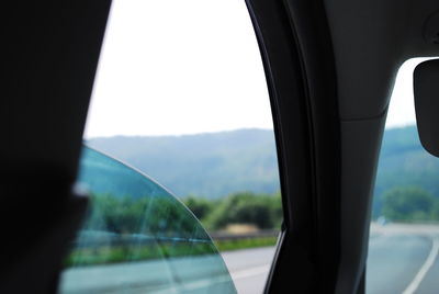 Close-up of side-view mirror against clear sky seen through car window