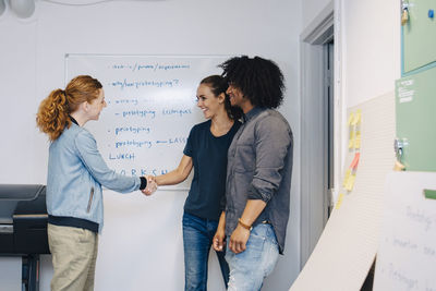 Businessman looking while standing by female colleagues greeting in creative office