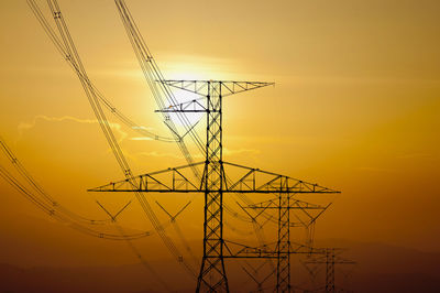 Low angle view of electricity pylon against sky during sunset