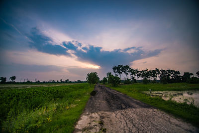 Road amidst field against sky during sunset