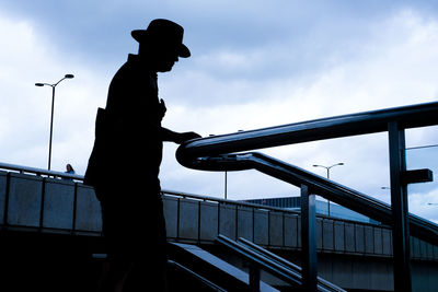 Silhouette man with hat standing on bridge against sky