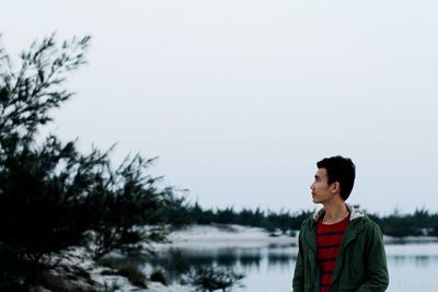 Young man standing by tree against clear sky