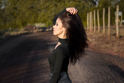 Side view of young woman with hand in hair standing on road