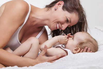 Close-up of happy young woman lying with baby on bed