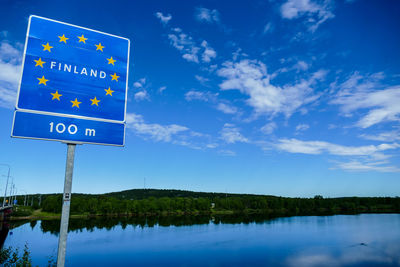 Information sign by lake against blue sky