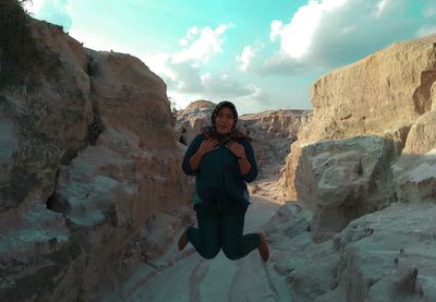 Full length of woman jumping on rock against sky