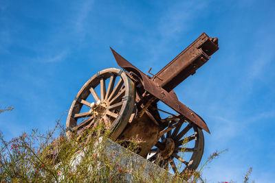 Low angle view of old rusty wheel against blue sky