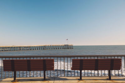 Empty benches on promenade by sea against blue sky