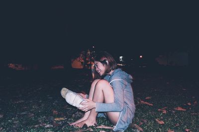 Side view of cheerful woman sitting with footwear on grass at park