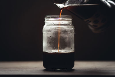 Close-up of coffee pouring in jar on table against black background