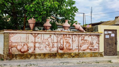 Graffiti on wall by potted plants against sky